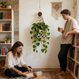 Cache pot en filet de coton blanc cassé avec une plante aux feuilles en cœur, dans un salon bohème avec deux personnes