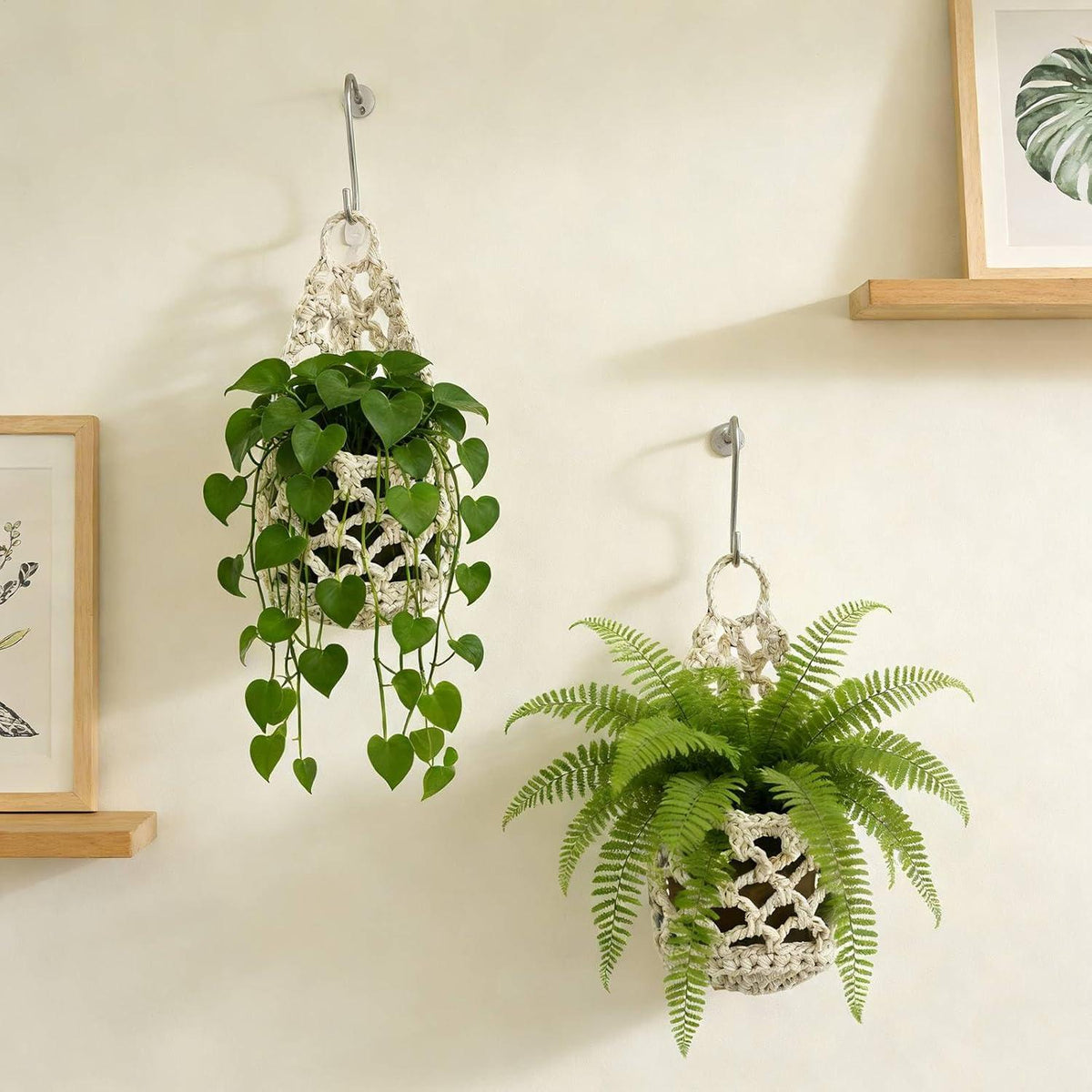 Deux cache pots en filet de coton blanc cassé accrochés à des crochets métalliques, avec une plante retombante et une fougère