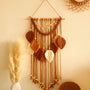 Tenture murale macramé Arcelle terracotta, arche tressée et feuilles, accrochée dans un salon avec des herbes de la pampa