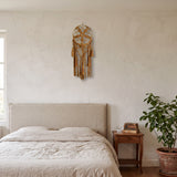 attrape rêve macramé ocre à fleur et glands, accroché au mur d'une chambre à la chaux, tête de lit en lin