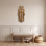 attrape rêve macramé ocre à fleur et glands, accroché dans une entrée à boiseries, au-dessus d'un banc en rotin