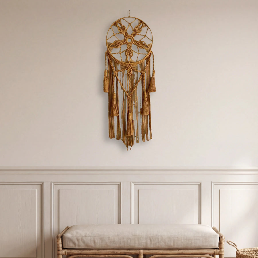 attrape rêve macramé ocre à fleur et glands, accroché au mur d'une entrée avec boiserie, au-dessus d'un banc en rotin