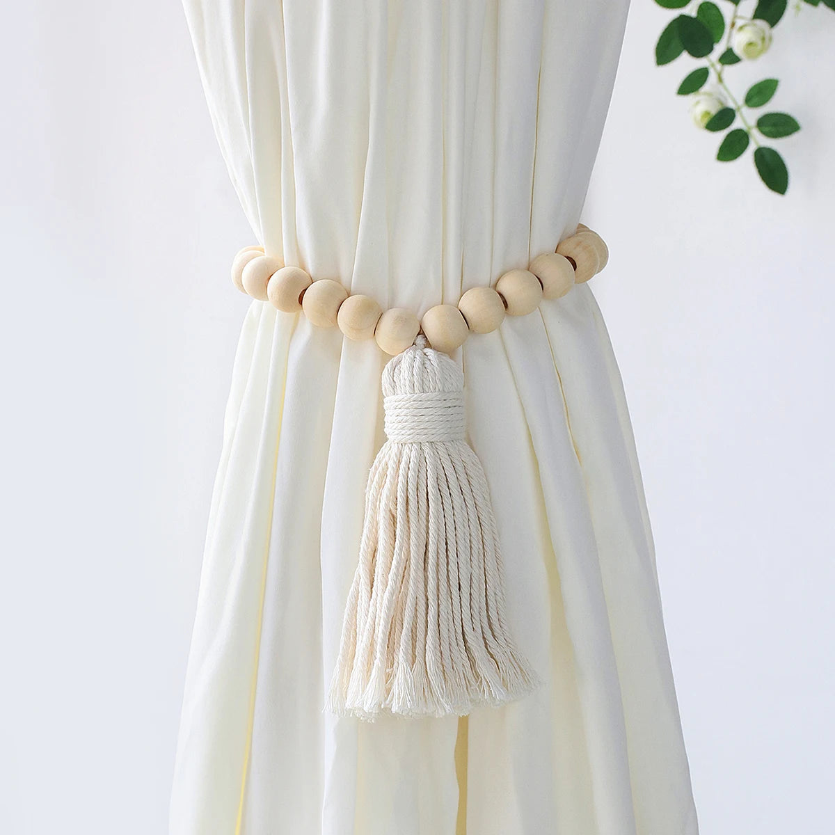 Embrasse rideau macramé feuille et pompon - perles en bois et pompon en coton sur rideau écru, feuillage derrière