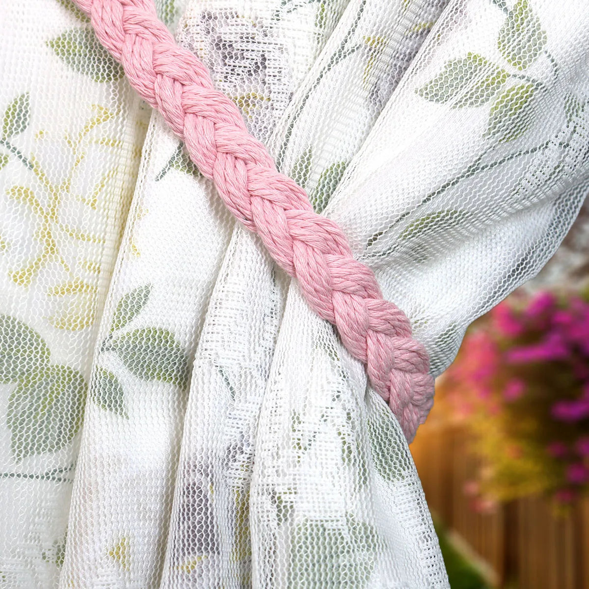Embrasse rideau tressée en coton rose pâle drapée autour d'un voilage blanc à motif floral, jardin flou