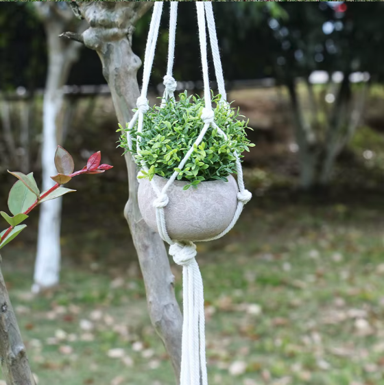 Porte-plante suspendu en macramé blanc avec un pot gris et une plante verte, en extérieur