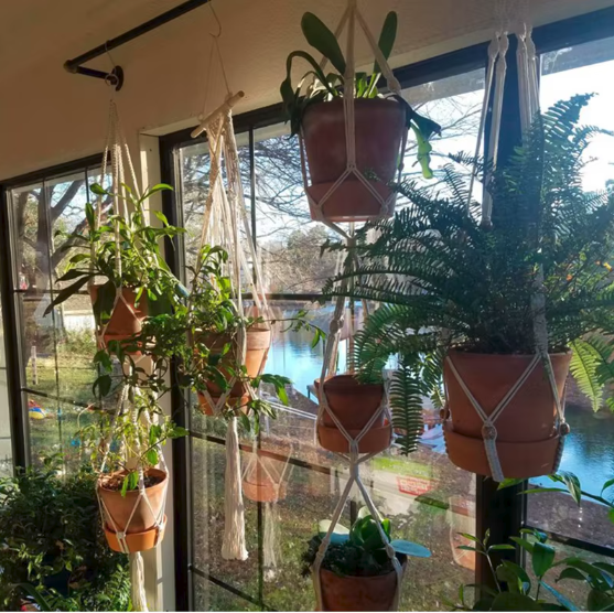 Plusieurs porte-plantes suspendus en macramé avec des pots en terre cuite devant une grande fenêtre
