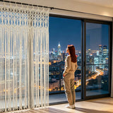 Rideau macramé bohème - devant une baie vitrée sur la ville de nuit, une femme de dos