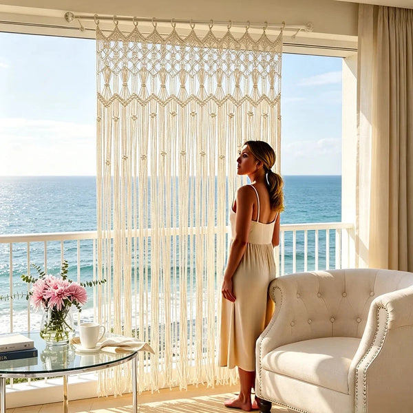 Rideau macramé bohème - devant un balcon, vue sur la mer et fauteuil capitonné, une femme regarde l'horizon