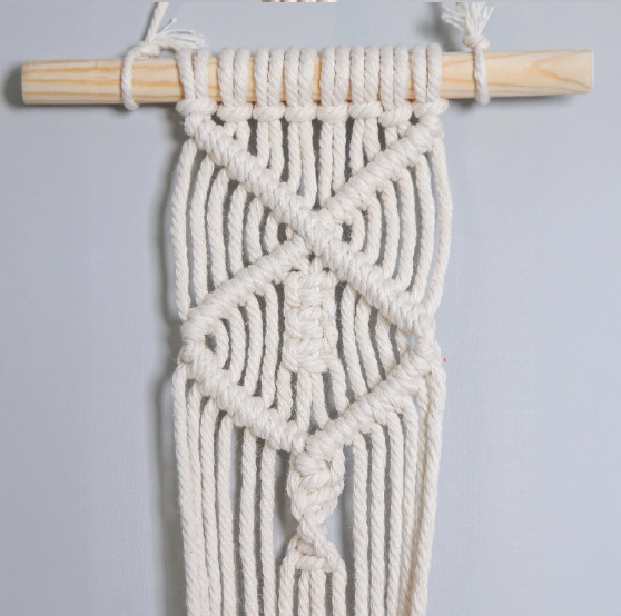 Suspension pot de fleurs macramé à bâton de bois, détail des motifs en croix et en losange sur un mur gris