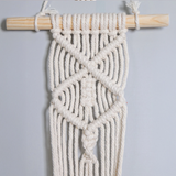 Suspension pot de fleurs macramé à bâton de bois, détail des motifs en croix et en losange sur un mur gris